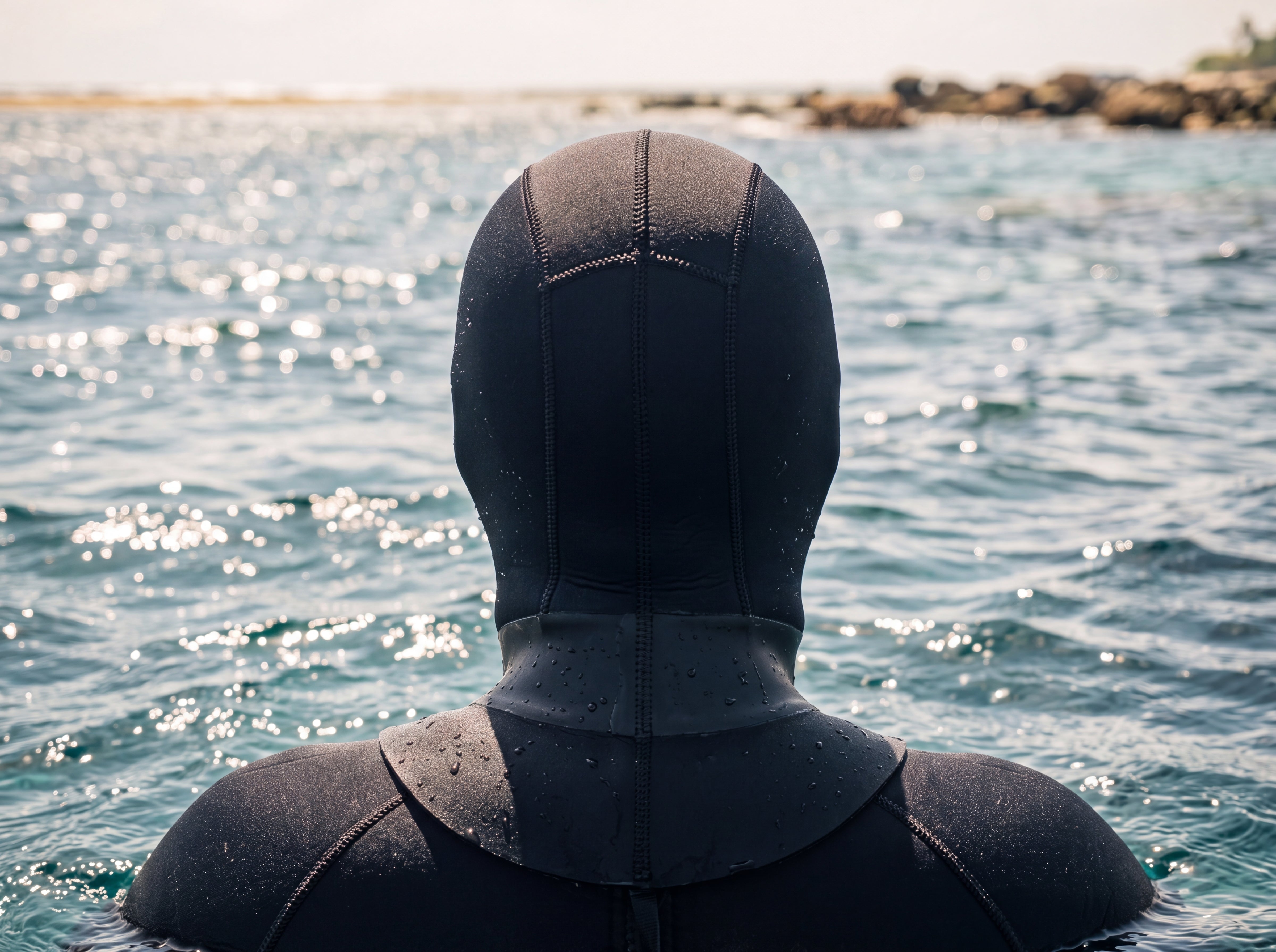 Diver at the surface wearing the Tilos 3mm Neoprene Dive Hood, viewed from behind toward the reef